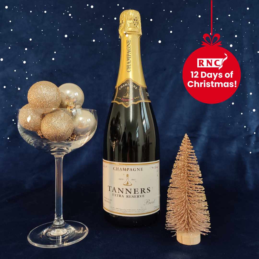 A bottle of Tanners champagne with a champagne saucer filled with gold baubles and a small glittery Christmas tree