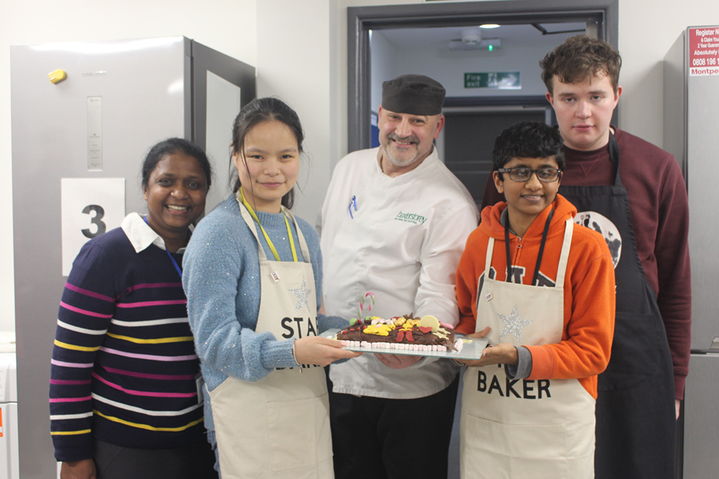 the star bakers stand holding their cake with the two judges and the event organiser