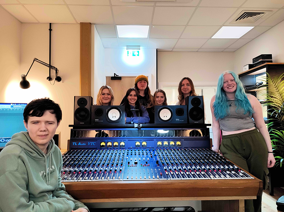 two RNC students are pictured with the HCA band around the mixing desk in the music studio