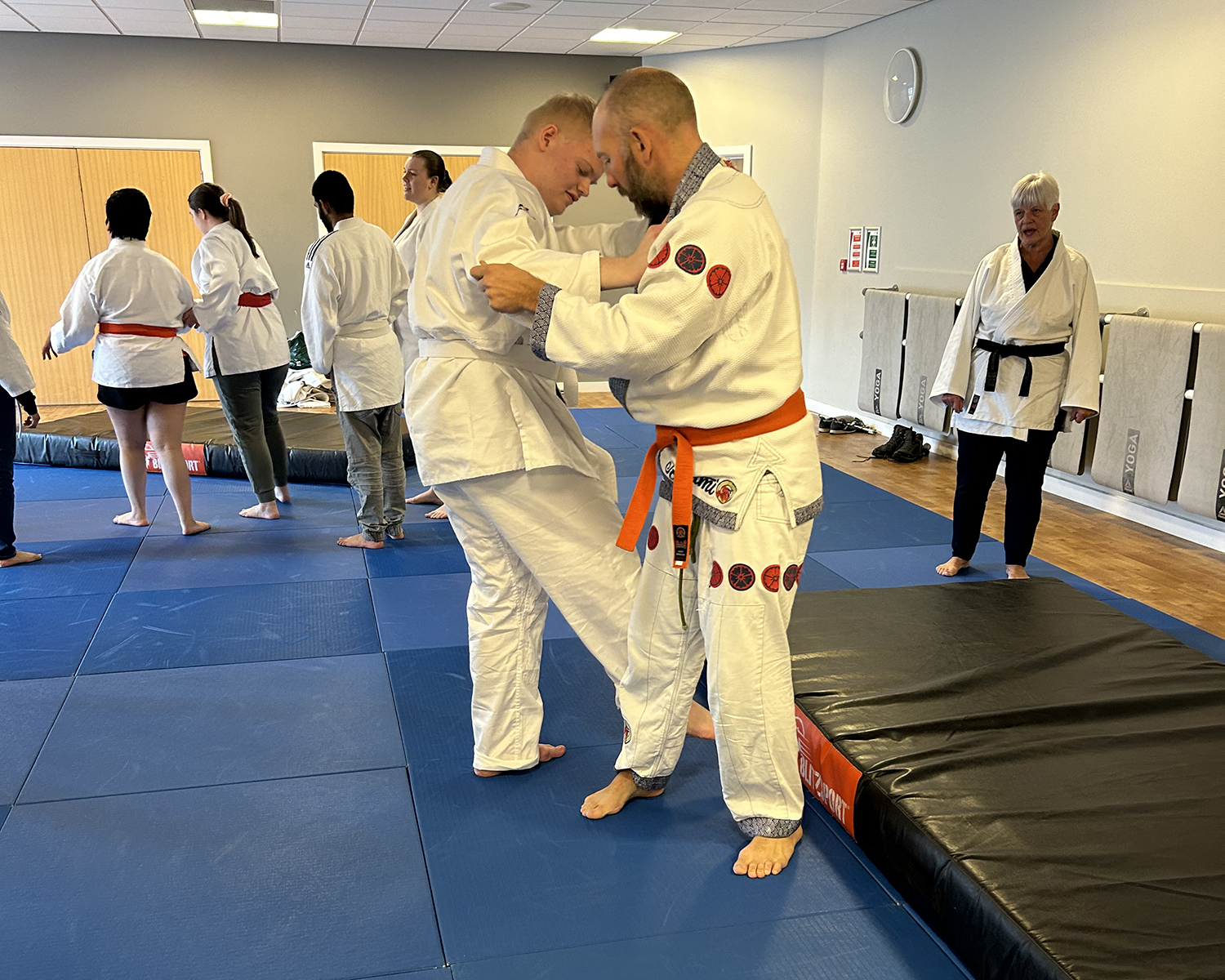 Phil demonstrating one of the throws with a student. Carol watches on and other students can be seen in the background 
